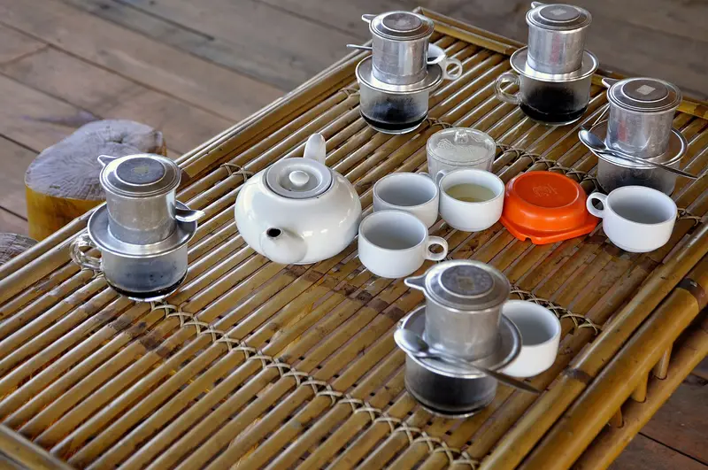 Aluminium phin filters dripping coffee into cups on a bamboo tray