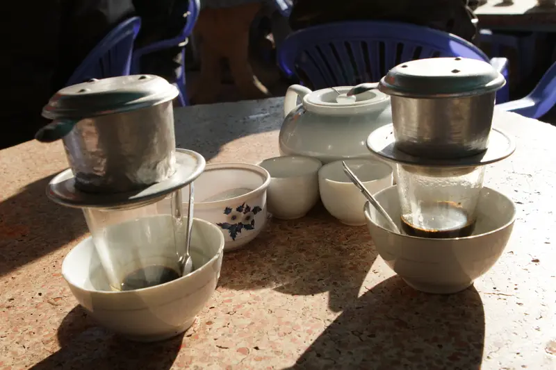Two phin filters dripping on a sunny café table